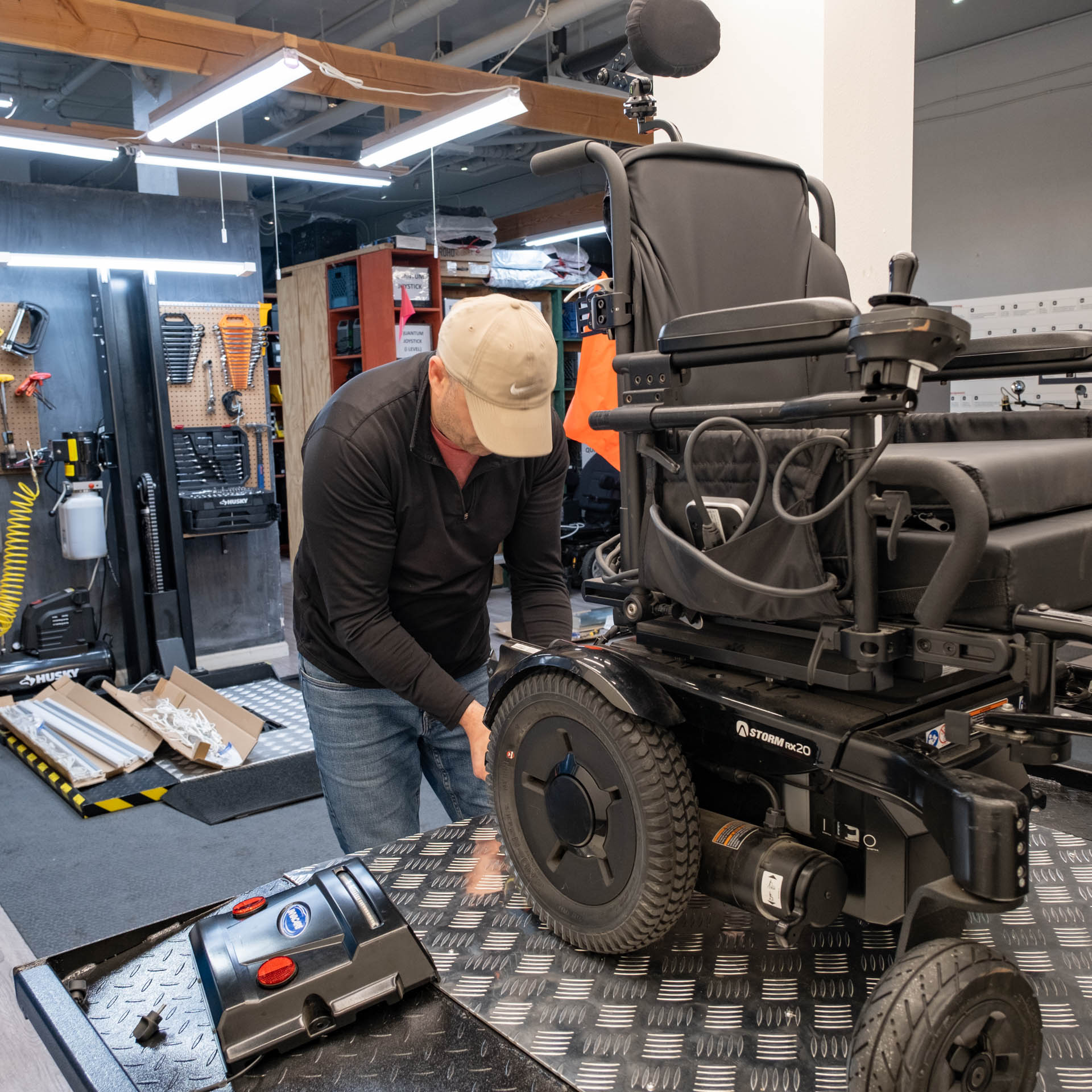 Levan works on a power chair using his new second wheelchair repair lift, with his original lift in the background.